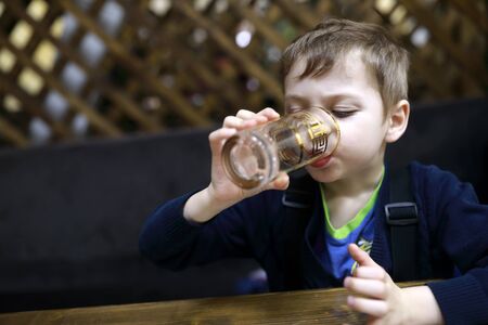 Child drinking water at table in restaurantの写真素材