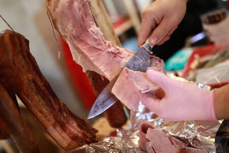 Person cuts slice of pork ham in market