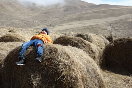 Child lies on bale of hay on farm, Kabardino-Balkaria, Russia