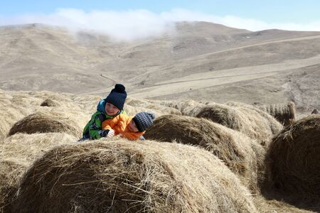 Boys playing on bale of hay on farm, Kabardino-Balkaria, Russia