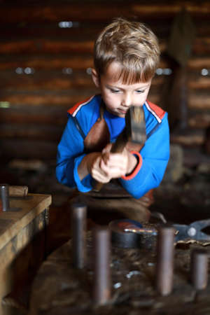 Kid learning to work with hammer in forgeの写真素材