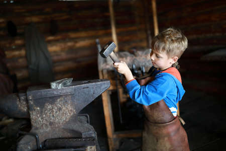 Child hits anvil with hammer in forgeの写真素材