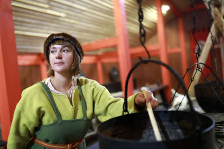 Viking woman cooking food in cauldron in hearthの写真素材