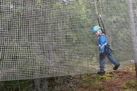Kid overcoming mesh obstacle in rope adventure park, Karelia
