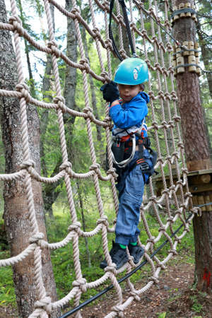 Boy overcoming mesh obstacle in forest adventure park, Karelia