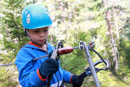 Boy learning to use carabiner in forest adventure park