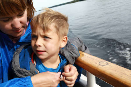 Mother buttons up her son jacket on deck of passenger ship