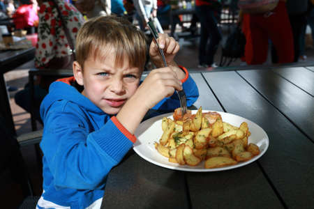 Child eating fried potatoes with meatballs in outdoor restaurant