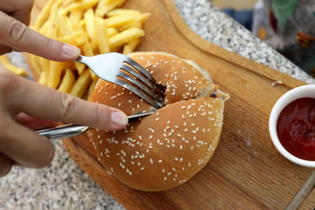 Person cuts burger on wooden board in restaurant
