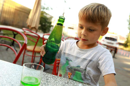 Child pouring green lemonade from bottle at restaurantの写真素材