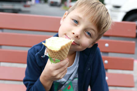 Boy has ice cream on wooden benchの写真素材