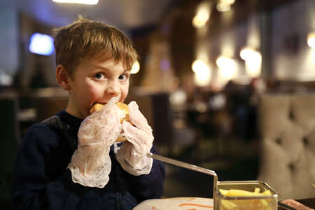 Boy with gloves eating burger in restaurantの写真素材