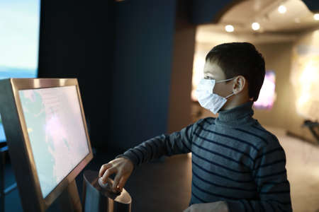 Kid in medical mask using touch screen in museumの写真素材