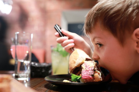 Portrait of child has burger in dark restaurant