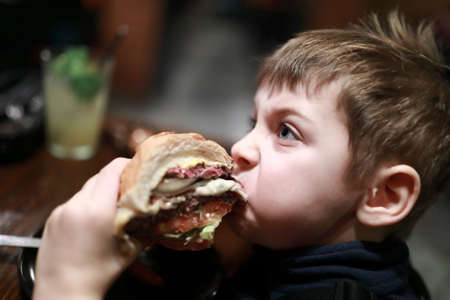 Portrait of boy has burger in dark restaurantの写真素材