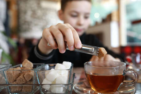 Kid taking piece of sugar with tongs in restaurant
