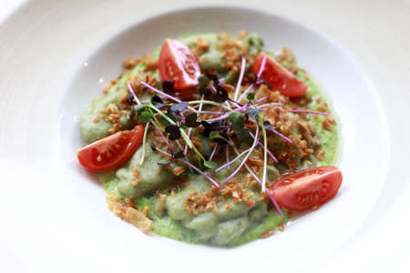 Dumplings with spinach and tomatoes on white plate in restaurant