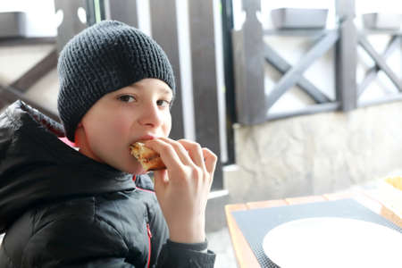 Boy eating slice of pizza on restaurant terrace