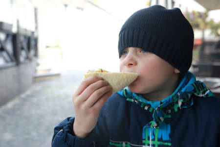 Child eating slice of pizza on restaurant terrace