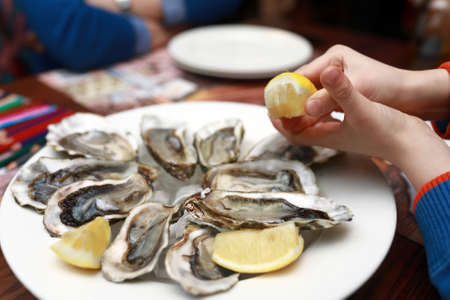 Person squeezes lemon juice onto oysters in restaurantの写真素材