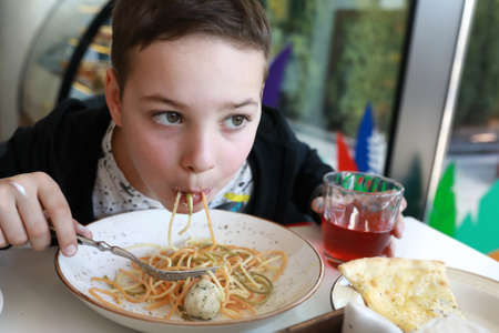 Boy has spaghetti with chicken meatballs in restaurant
