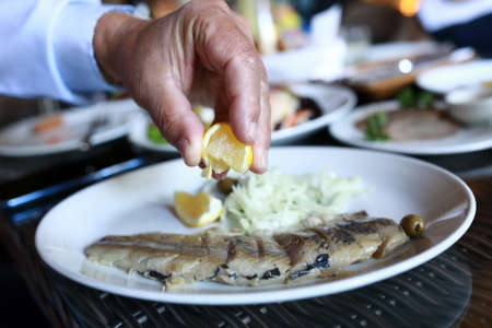 Person squeezes lemon juice on salted herring in restaurant