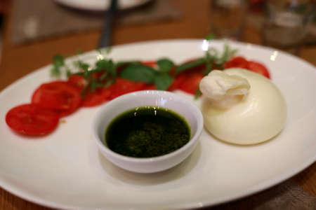 Burrata cheese with tomatoes and sauce on plate in restaurantの写真素材