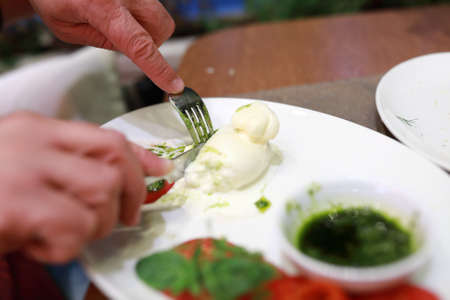 Person cutting Burrata cheese on plate in restaurantの写真素材