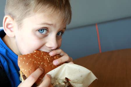 Hungry boy has burger in a restaurantの写真素材