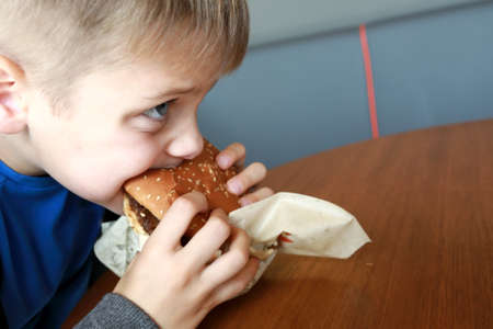 Hungry kid eating burger in a restaurant