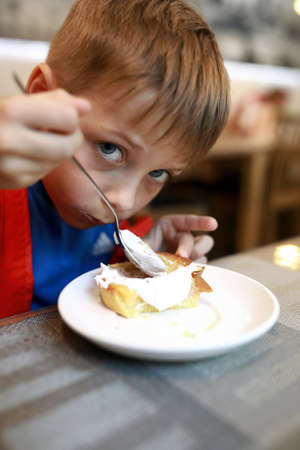 Boy eating cheesecake with sour cream in restaurantの写真素材