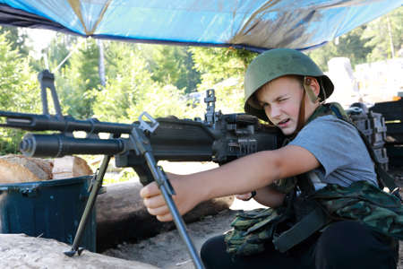 Boy in military helmet with machine gun in parkの写真素材