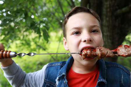 Boy eating pork neck kebab on skewers in parkの写真素材