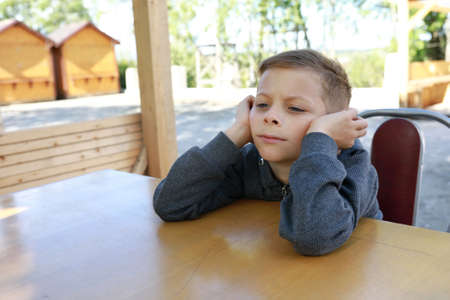 Pensive kid waiting food at table in restaurantの写真素材
