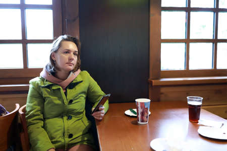 Thinking woman with smartphone at table in restaurantの写真素材
