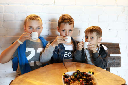 Three children drinking tea at round wooden tableの写真素材