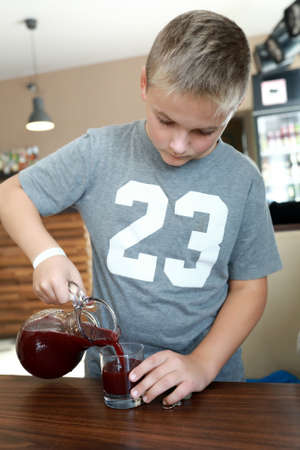Boy pouring juice from carafe in restaurantの写真素材