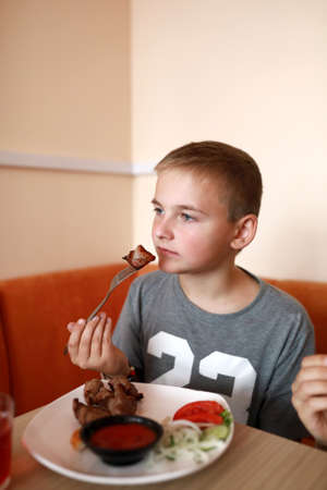 Child eating pork kebabs with vegetables in restaurantの写真素材