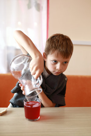 Kid pouring juice into glass in restaurantの写真素材