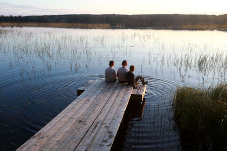 Brothers resting on wooden bridge by lake at sunset, Kareliaの写真素材