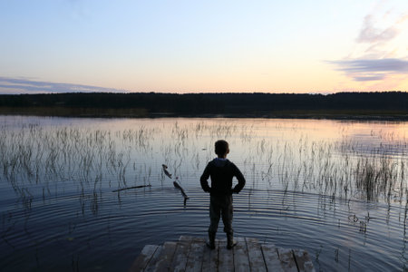Child standing on wooden bridge by lake at sunset, Kareliaの写真素材