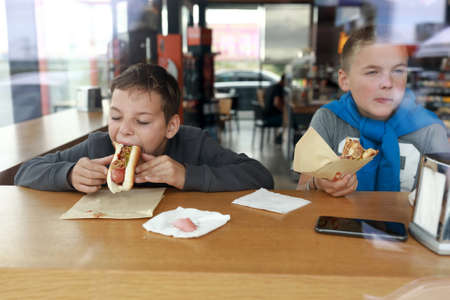 Portrait of two children eating Hot Dog in restaurantの写真素材