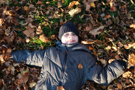 Child lying on autumn leaves in parkの写真素材