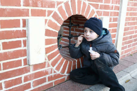 Portrait of child sitting on sidewalk by buildingの写真素材