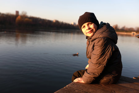 Portrait of child sitting by lake at sunsetの写真素材