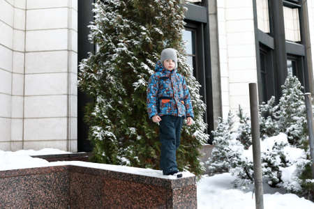 Portrait of boy on curb of building in winterの写真素材
