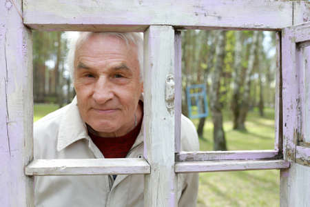 Senior man looking through wooden frame in parkの写真素材