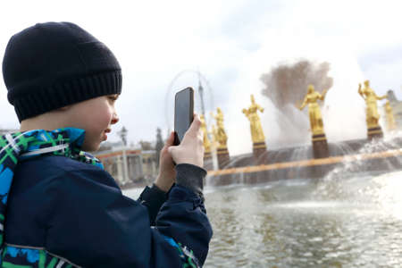 Child takes photo of fountain with smartphone in parkの写真素材