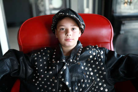 Portrait of child in leather jacket and cap sitting on chair