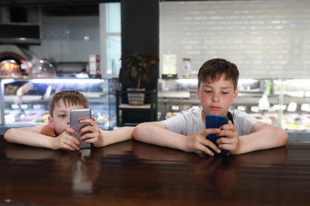 Children playing with smartphones at bar in restaurantの写真素材